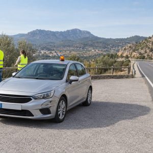 Coche detenido en un apartadero con baliza luminosa y dos viajeros alejados de la carretera